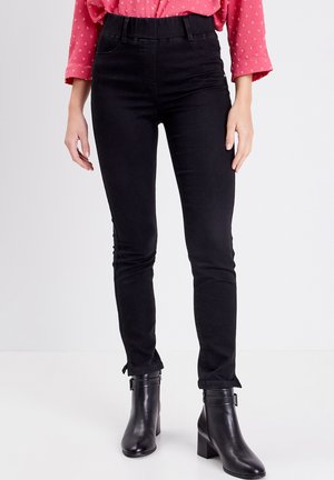 Jean skinny noir avec taille haute, en denim extensible. Associé à des bottines noires avec détail de boucle.