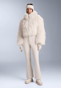 Biała krótkia kurtka z puszystą teksturą, wysoki kołnierz, w połączeniu z beżowymi rozszerzanymi spodniami. Dodatki to pasujące rękawiczki i opaska na głowę. Gładka faktura.