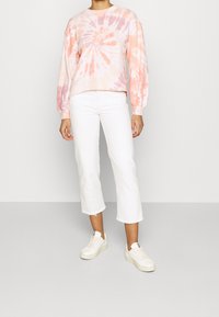 Felpa pullover tie-dye rosa chiaro con collo rotondo e maniche lunghe, abbinata a jeans bianchi a vita alta e sneakers bianche. Texture morbida.