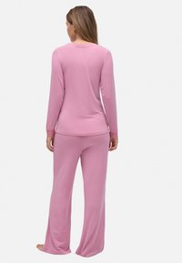 Parte superior de color rosa claro de manga larga y pantalones a juego hechos de un tejido suave. La parte superior presenta detalles de encaje en los puños; diseño de corte holgado.