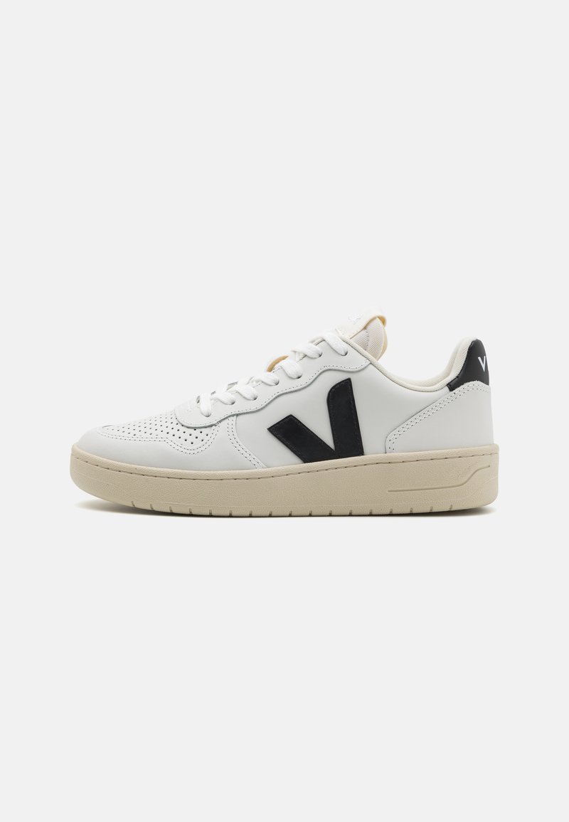 Hvit lær sneakers med svart logo, perforert tåområde og beige gummisåle. Har en jevn tekstur og snøring.