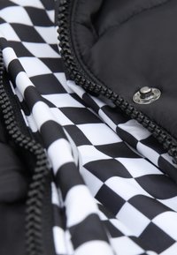 Nærbillede af sort-hvid ternet stof indeni et sort quiltet beklædningsstykke med lynlås og metal trykknap.