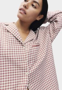 Chemise à boutons dans un motif à carreaux rose et crème, dotée d'un col, de manches longues et d'une poche poitrine avec un accent subtil.