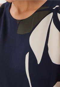Laivastonsininen paita, jossa on suuret valkoiset ja oliivinvihreät kukkakuviot, pyöreä kaula-aukko ja sileä rakenne.