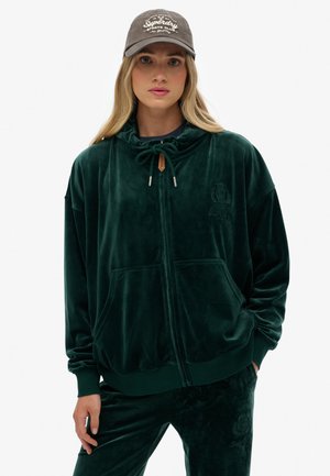 Haut à capuche zippé en velours vert avec un col à cordon, des poches avant et une broderie de logo. Assorti avec un pantalon en velours pour un look coordonné.