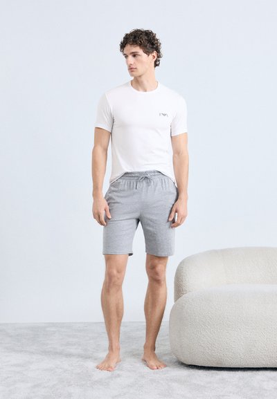 Wit shirt met korte mouwen en logo, gecombineerd met grijze shorts met elastische tailleband. Eenvoudig ontwerp, gladde textuur, staand op een licht tapijt.
