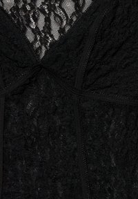 Țesătură din dantelă neagră cu modele florale și detalii din plasă transparentă, având linii de cusătură și broderie texturată.