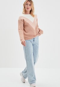Maglione lavorato a maglia rosa chiaro e crema con un motivo a V, texture a coste e maniche lunghe, abbinato a jeans a gamba dritta azzurri.