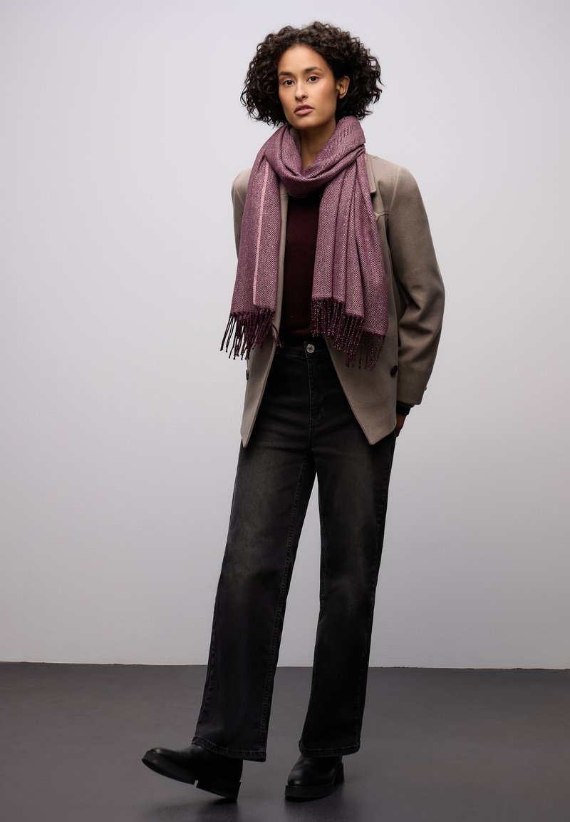 Purple woven scarf with fringes, worn over a maroon top and gray blazer, paired with high-waisted black jeans and black ankle boots.
