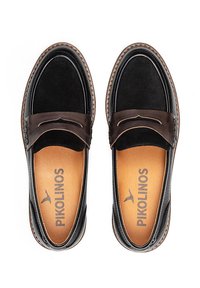 Mocasines de cuero negro con un acento de cuero marrón, detalles de costura y una textura suave. La plantilla interna presenta la marca "Pikolinos".