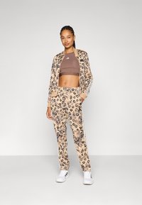 Leopardmønstret treningsdress i beige og brunt, med stripete detaljer, en tettsittende brun crop top og hvite sko.