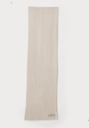 Beige ribots adīts šalle, izgatavota no mīksta materiāla. Raksturīga smalka logotipa birka apakšā. Gara un taisnstūra forma.