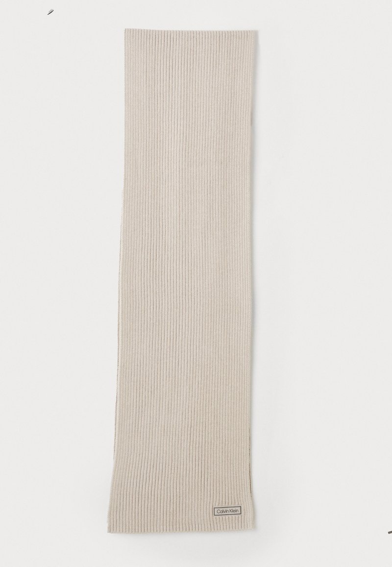 Bufanda de punto acanalado beige fabricada con material suave. Cuenta con una etiqueta de logo sutil en la parte inferior. Tiene forma larga y rectangular.