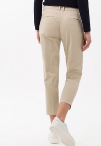 Beige cropped broeken met een soepele textuur, riemlussen en twee achterzakken. Draag het met witte instapsneakers.