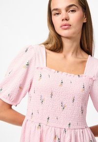 Roza, teksturirana obleka s kratkimi napihnjenimi rokavi, kvadratnim izrezom in cvetličnim vezenjem v rumeni in vijolični barvi na nabranem korzetu.