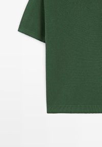 Kortærmet skovgrøn trøje i strikket stof med ribbet kant ved forneden og ved ærmekanter, vist mod en hvid baggrund.