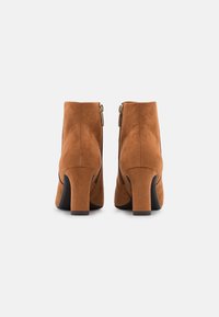 Bottes basses en daim marron avec un bout arrondi, un talon épais et des fermetures éclair sur les côtés. Texture lisse avec peu de détails.