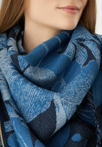 Écharpe bleue en tissu tissé avec des motifs floraux dans différentes nuances de bleu et de noir, avec une finition texturée et des plis épais et doux.