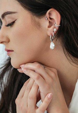 Silver earrings, including a pearl drop, flower design, and small stud, worn by a person with long hair, showcasing various textures and shapes.