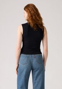 Top negru fără mâneci, cu un design ajustat, combinat cu blugi de un albastru deschis, cu talie înaltă și buzunare cusute pe spate. Textură de țesătură netedă.