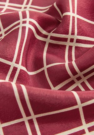 Piros szövet krémszínű rácsos mintával, lágy redőkkel és sima textúrával.