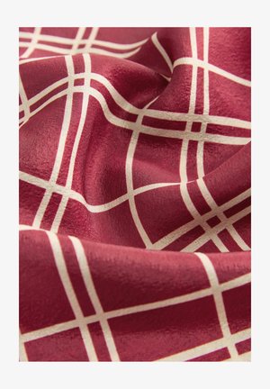 Červená látka s krémovou mriežkovou štruktúrou, ukazujúca jemné záhyby a hladkú textúru.