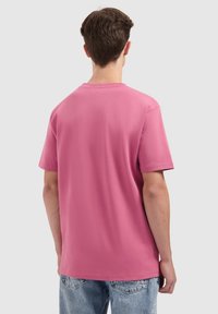 Roze T-shirt met korte mouwen van katoen met een relaxte pasvorm; heeft een ronde hals en een effen achterkant. Gekleed met lichtblauwe jeans.