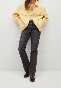 Gul uldblandingsjakke med to forlommer, hvid top og højtaljede mørke grå jeans. Sorte ankelstøvler med en glat finish.