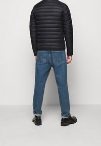 Czarna kurtka puchowa z poziomymi przeszyciami, w zestawie z niebieskimi spodniami typu straight leg i czarnymi masywnymi butami, widok z tyłu.