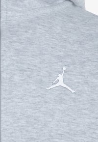 Grå fleece hettegenser med en teksturert overflate, med en hvit Jumpman-logo på brystet. Materialet er mykt og glatt.