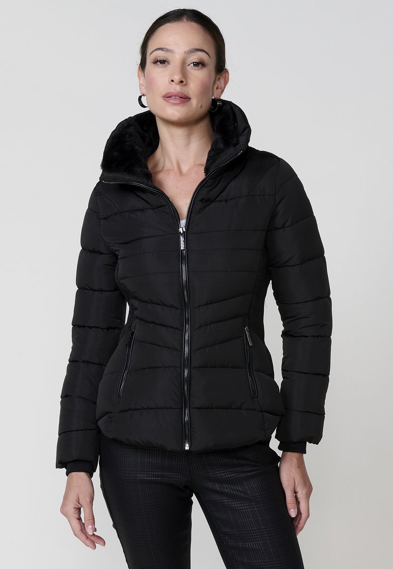 Chaqueta negra acolchada con cierre frontal, capucha forrada de piel sintética y puños de canalé. Presenta un diseño acolchado y bolsillos laterales con cremallera.