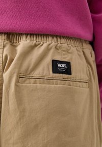 Khaki shorts lavet af bomuld med elastisk talje, med en baglomme og et sort Vans mærkelabel. Toppen er en pink sweatshirt.