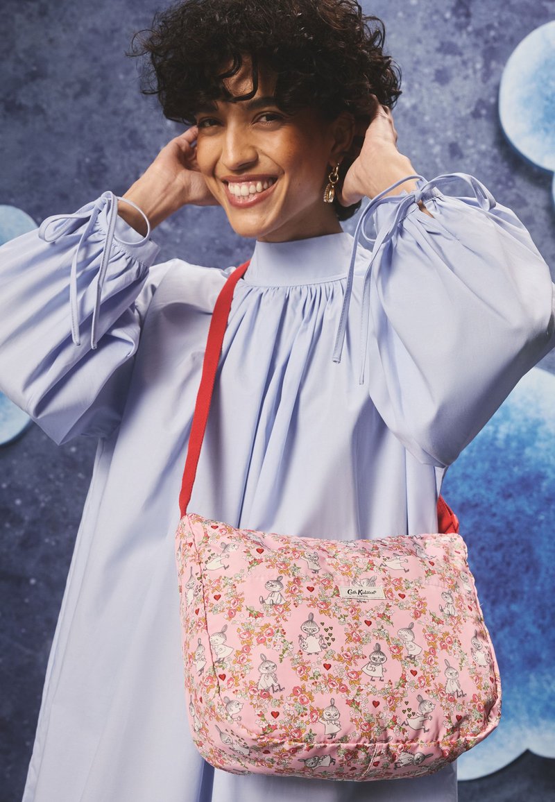 Růžová vzorovaná kabelka přes rameno s květinovým motivem a kreslenými postavičkami. Měkká látka, zaoblený tvar a červený popruh pro nošení přes tělo.