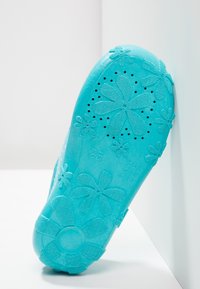 Turquoise plastic schoenolka met bloempatronen, een gestructureerde grip en ventilatiegaten. Duidelijke maatmarkering "25" nabij de hiel.
