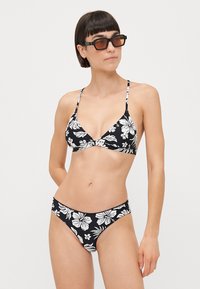 Svart bikini med hvite blomster mønster; har en trekantet topp med tynne stropper og en lavt liv bukse med et lignende design.