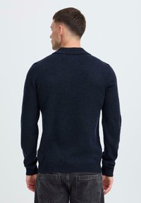 Navyblauer Strickpullover mit langen Ärmeln und einem umgeschlagenen Kragen, der aus einem strukturierten Stoff gefertigt ist und eine leicht taillierte Passform in der Taille hat.