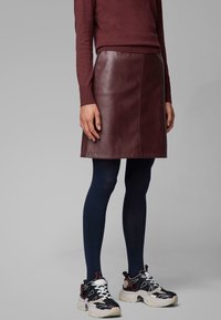 Burgunderfärgad läder A-linjeformad kjol med sömdetaljer, matchad med marinblå strumpbyxor och svarta sneakers med vita accenter och kraftig sula.