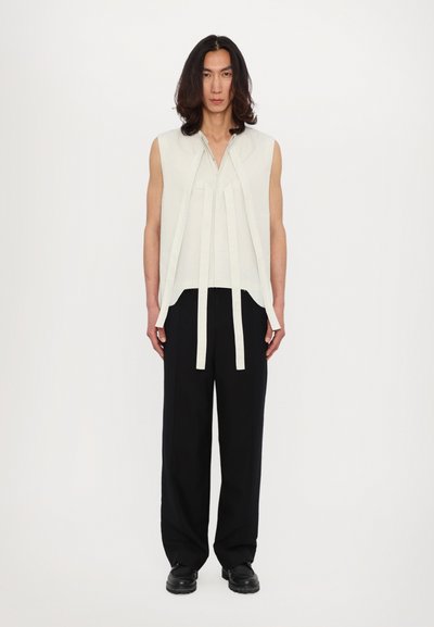 Top bianco senza maniche con lacci frontali, abbinato a pantaloni neri larghi. Tessuto liscio con dettagli minimi, che offre una silhouette rilassata.