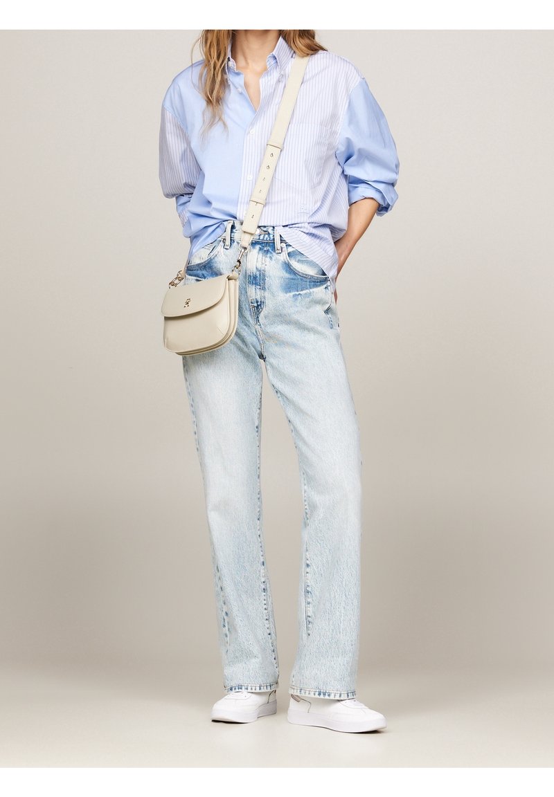 Světle modrá pruhovaná košile s knoflíky, volné světle modré džíny a bílé slip-on boty. Malá béžová kabelka přes rameno s klopou.