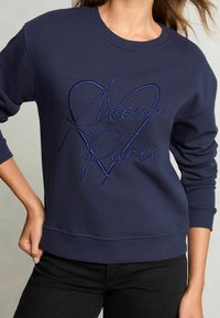 Felpa blu navy con collo a giro, caratterizzata da un testo ricamato "Amour Paris" in blu scuro, materiale testurizzato e polsini a coste.