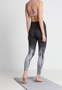 Legginsy w czarno-szarym ombre z wysokim stanem, w zestawie z różowym stanikiem sportowym z krzyżującymi się plecami. Widoczna miękka, elastyczna tkanina.