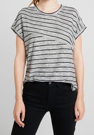 Woman wearing a short-sleeve, gray heathered t-shirt with black horizontal stripes and high-waisted black pants against a gray background.