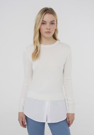 Maglietta a maniche lunghe con corpo in maglia bianca e pannello inferiore bianco con bottoni, caratterizzata da un scollo rotondo e una vestibilità aderente.