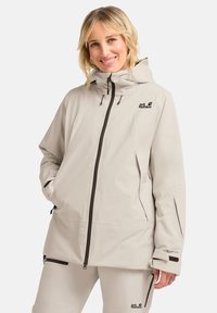 Veste imperméable beige clair avec capuche, dotée d'une fermeture éclair à l'avant, de poches latérales et d'accents de logo. Fabriquée en matériau TEXAPORE durable.