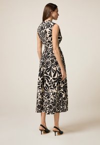 Schwarzes und weißes Blumendruckkleid mit ärmellosem Design, tailliertem Schnitt und fließendem Rock; kombiniert mit schwarzen, offenen, hochhackigen Schuhen.