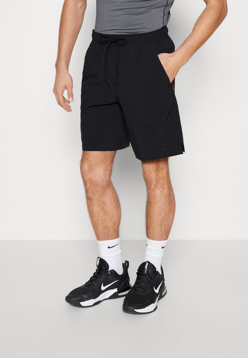 Shorts de sport noirs avec une taille élastique et un cordon de serrage, dotés de poches latérales et d'un petit logo. Portés avec des baskets noires et des chaussettes blanches.
