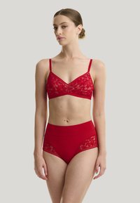 Bralette in pizzo rosso con spalline regolabili e bordo scallopato, abbinato a slip rossi a vita alta con dettagli in pizzo e una cintura liscia.