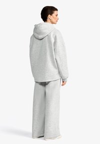 Felpa oversize grigia chiara con cappuccio e maniche ampie, abbinata a pantaloni sportivi a gamba larga dello stesso colore. Tessuto morbido e testurizzato senza fantasie.