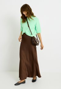 Pull en peluche vert clair ; jupe maxi satinée marron ; ballerines noires avec des clous blancs ; petit sac à bandoulière à motifs ; tenue décontractée.