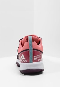 Zapatilla deportiva rosa con una parte superior texturizada, detalles blancos y una lengüeta azul claro en el talón. Cuenta con una suela acolchada y detalle del logo.